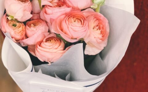 person wearing red sweater and black pants holding bouquet of pink flowers