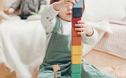 child in white long sleeve top and dungaree trousers playing with lego blocks