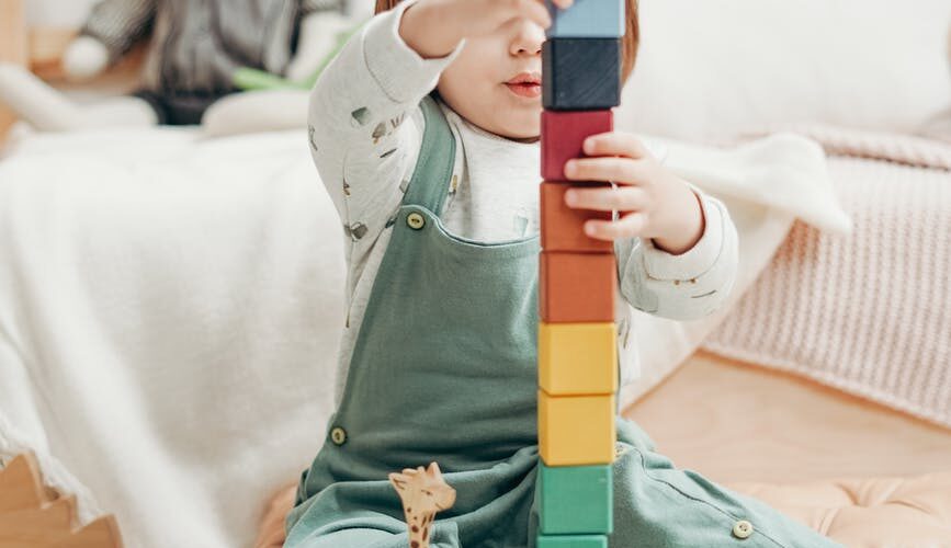 child in white long sleeve top and dungaree trousers playing with lego blocks