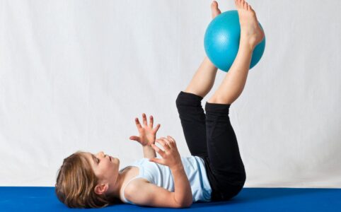 girl in white shirt and black pants lying on blue exercise ball