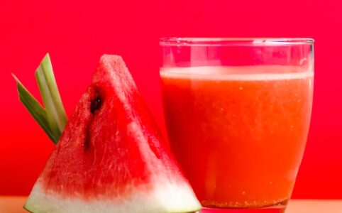 watermelon shake filled glass cup beside sliced watermelon fruit on brown surface