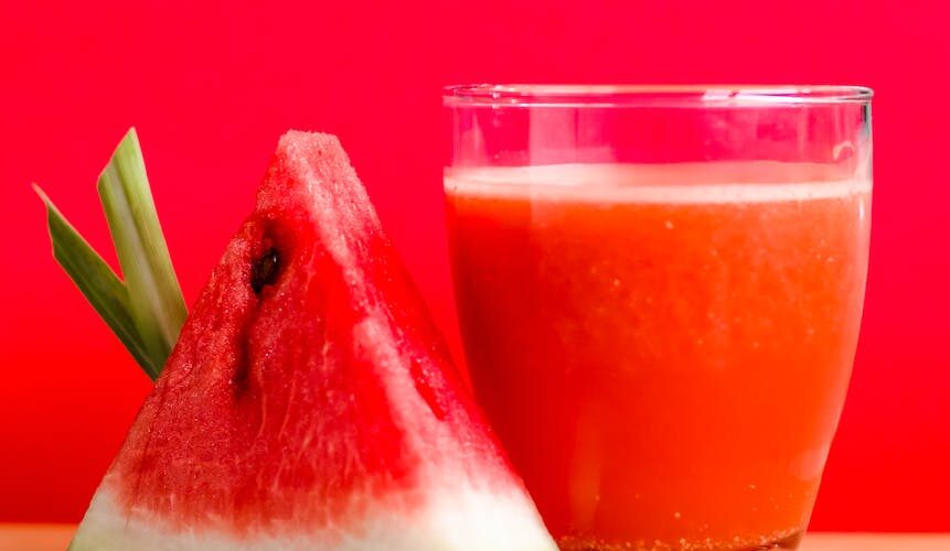 watermelon shake filled glass cup beside sliced watermelon fruit on brown surface