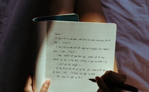 crop lady with pen and notebook on bed at home