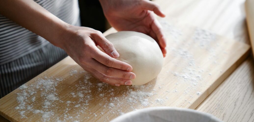 hands holding dough on cutting board